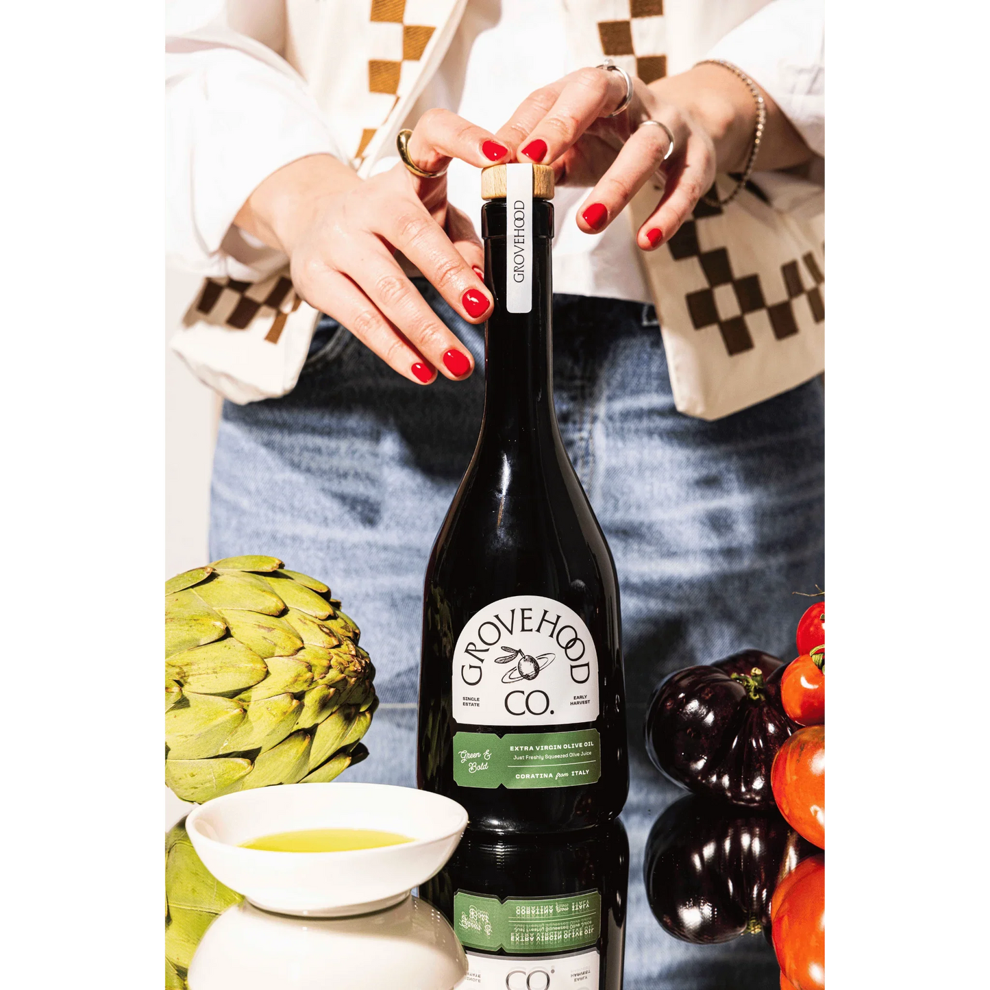 Grovehood Collective Italian extra virgin olive oil bottle at a table with tomatoes and artichoke