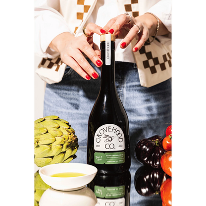 Grovehood Collective Italian extra virgin olive oil bottle at a table with tomatoes and artichoke
